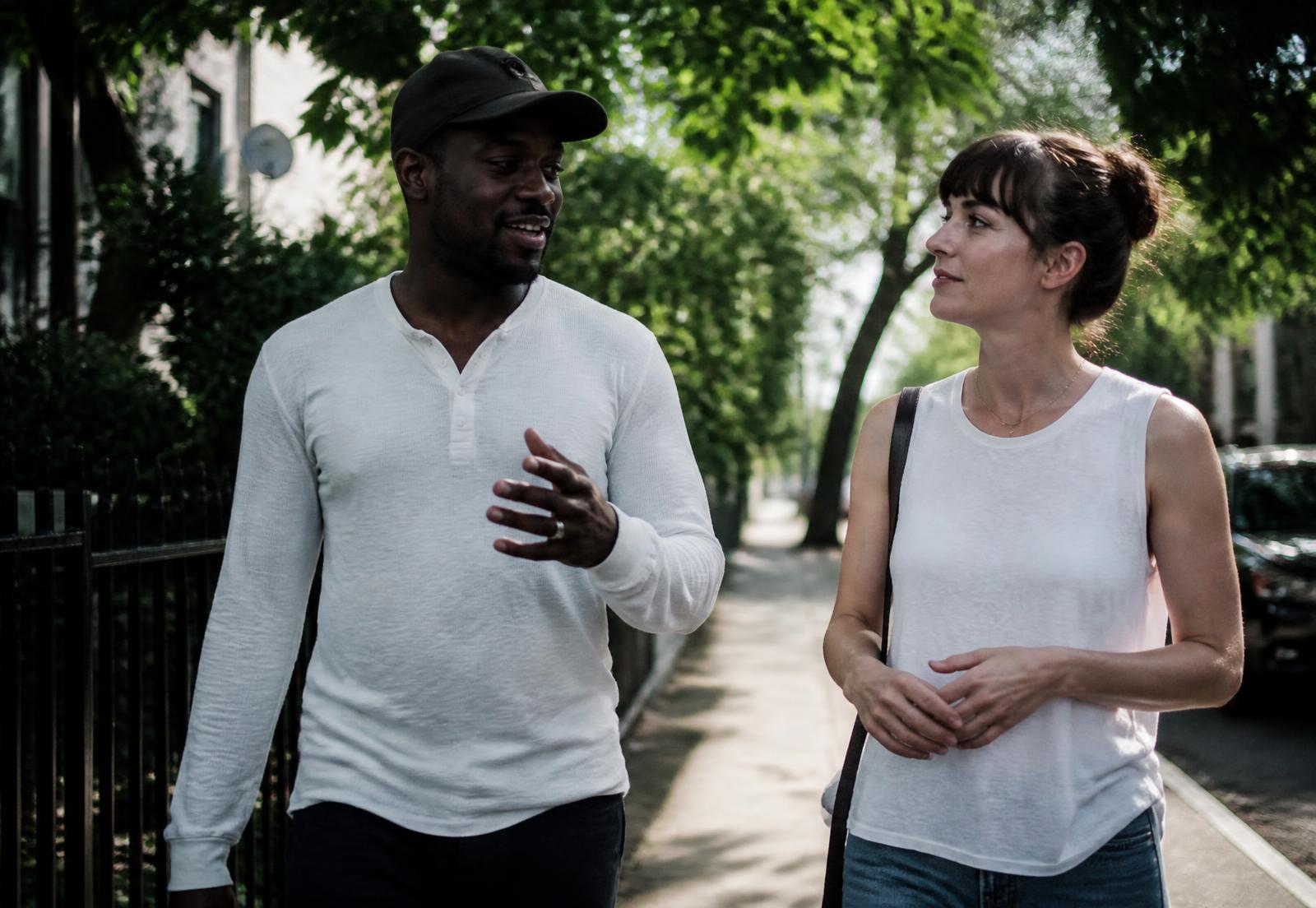 Two people walking and talking along a tree-lined neighbourhood street